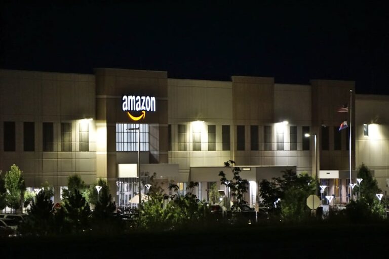 Amazon warehouse building illuminated at night with trees and signage.